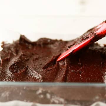 Brownie batter being spread in glass pan.