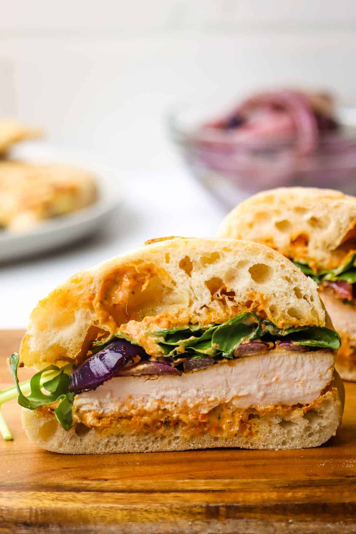 A grilled chicken sandwich sliced in half to show the inside on a wooden cutting board.