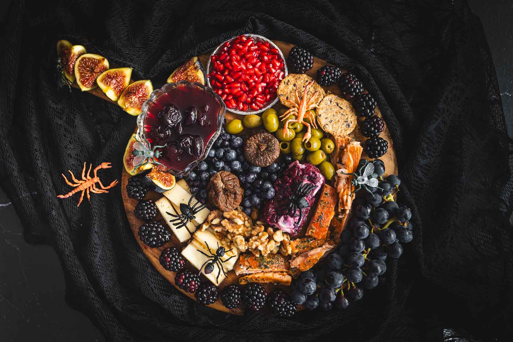 A halloween snack board full of cheese and fruit on a black background.
