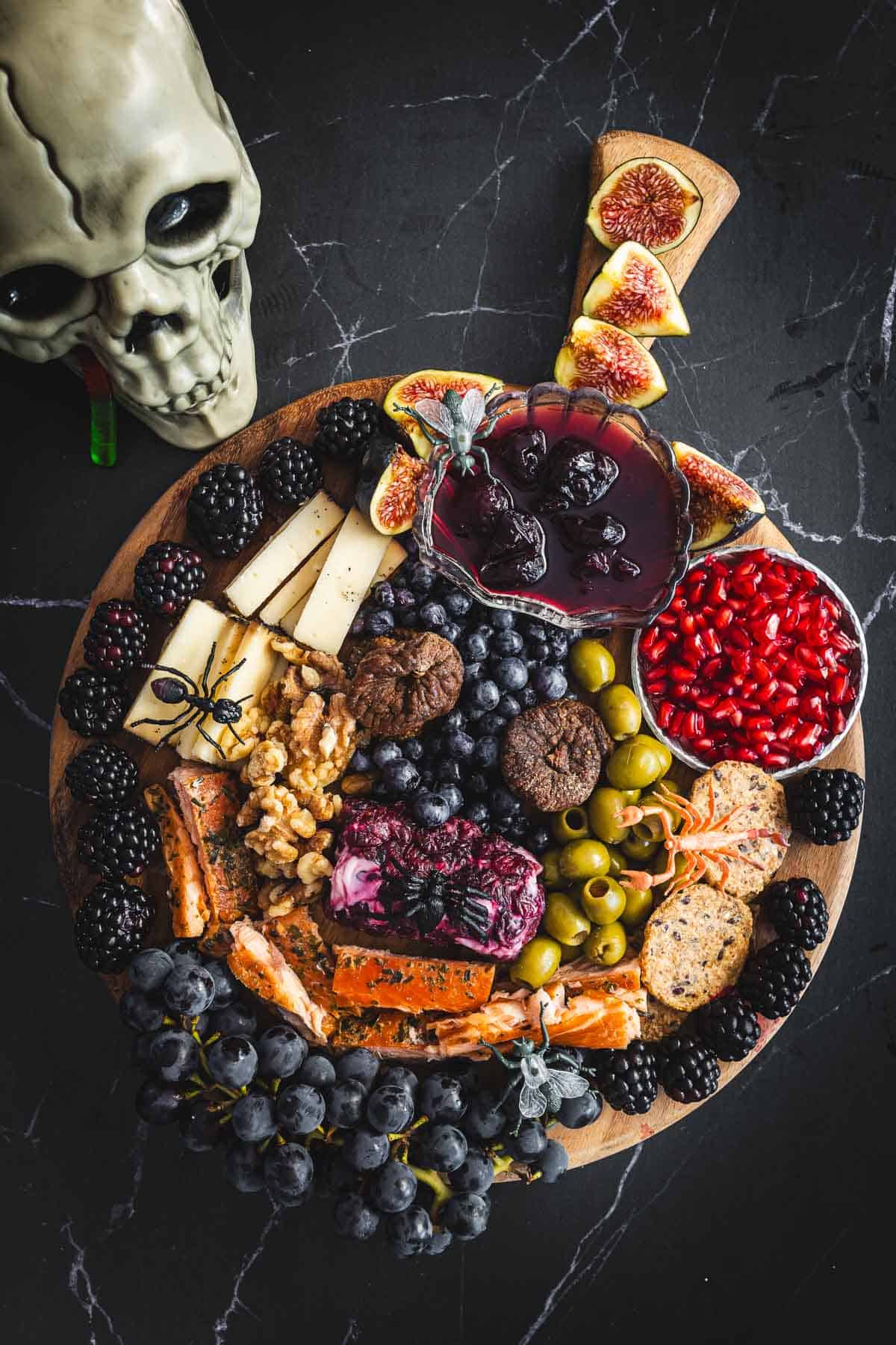 A halloween snack board full of cheese and fruit on a black background.