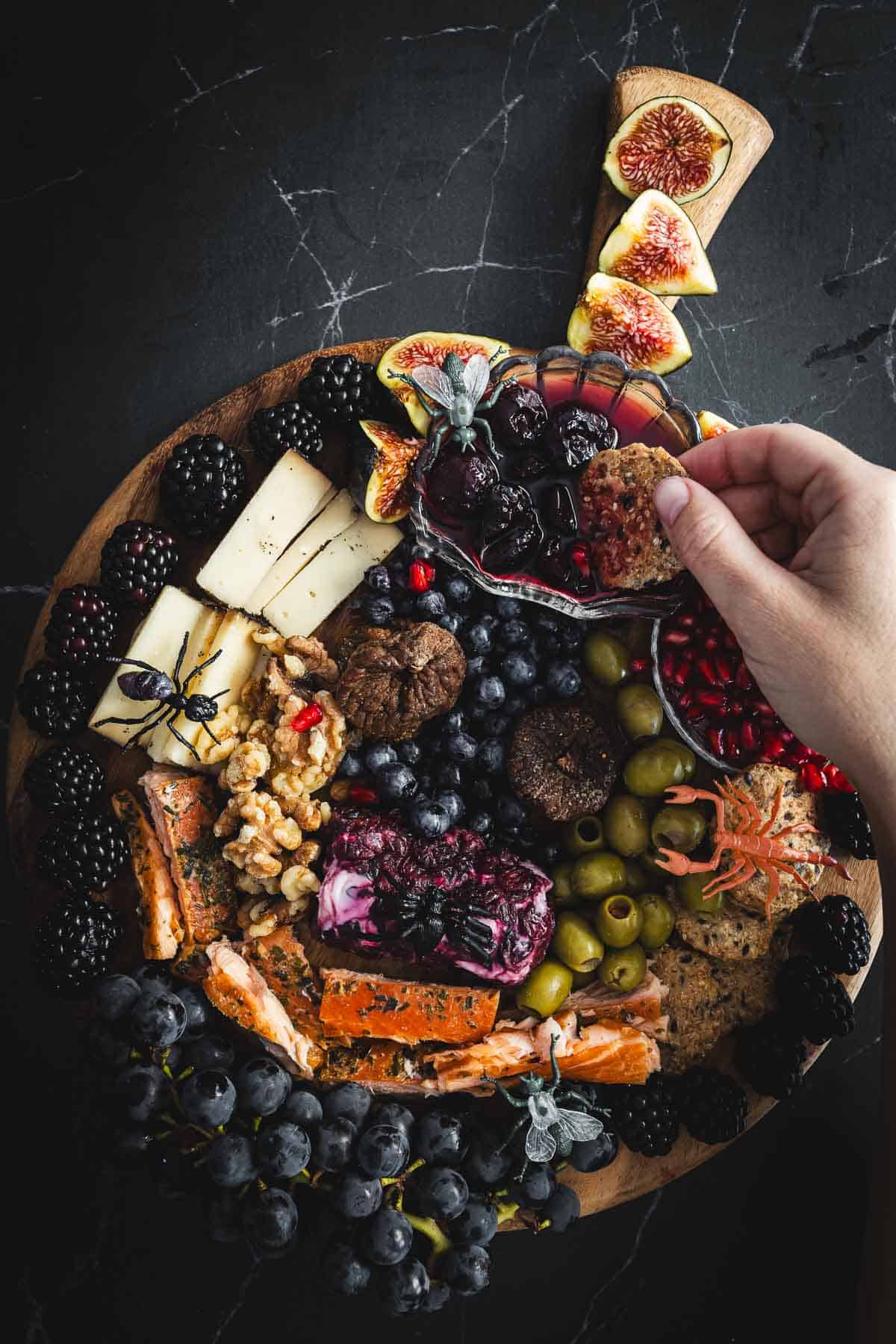 A hand holding a platter of fruit and cheese.