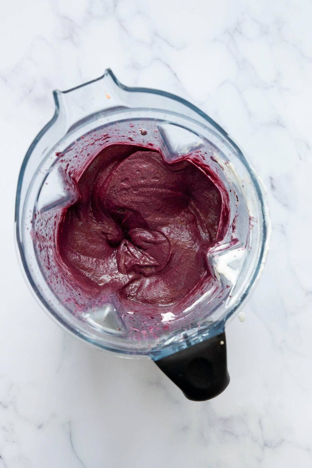Thick acai smoothie in a blender before adding to a bowl with toppings.