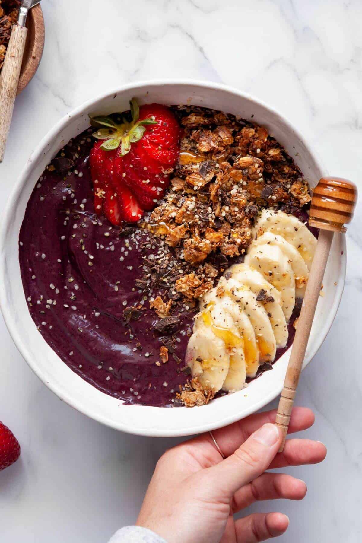 Homemade high protein Acai bowl with coco nibs, granola, strawberries, banana slices, honey, and hemp hearts.
