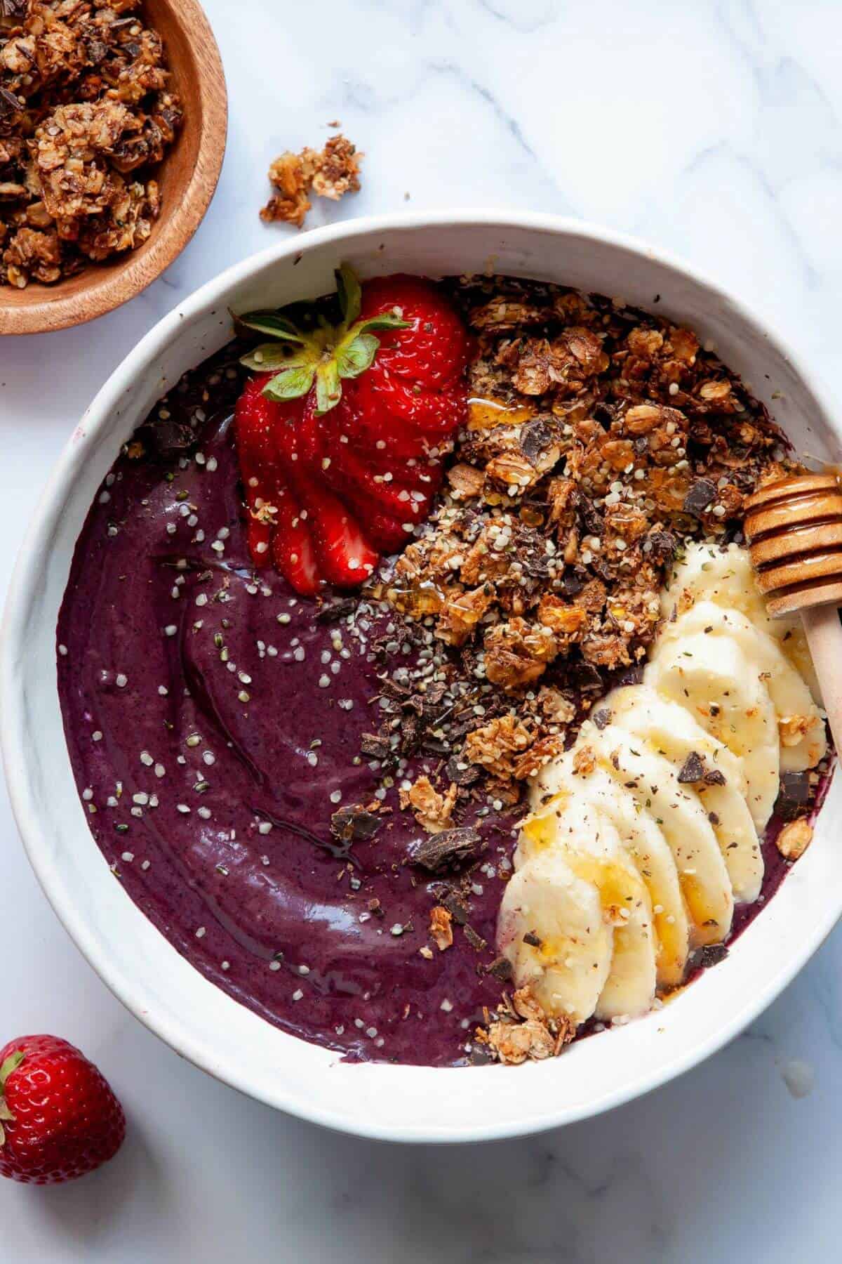 5 minute healthy, homemade high protein Acai bowl with granola, banana slices, honey, and sliced strawberries on top.