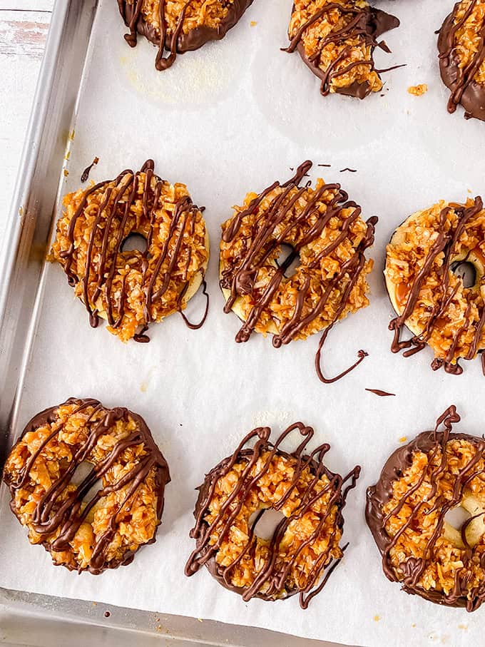 Homemade Samoas featuring cookies with caramel, coconut, and rich chocolate drizzles rest enticingly on a parchment-lined baking sheet.