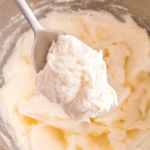 A metal spoon holds a scoop of creamy, whipped marshmallow frosting above a mixing bowl filled with more easy frosting.