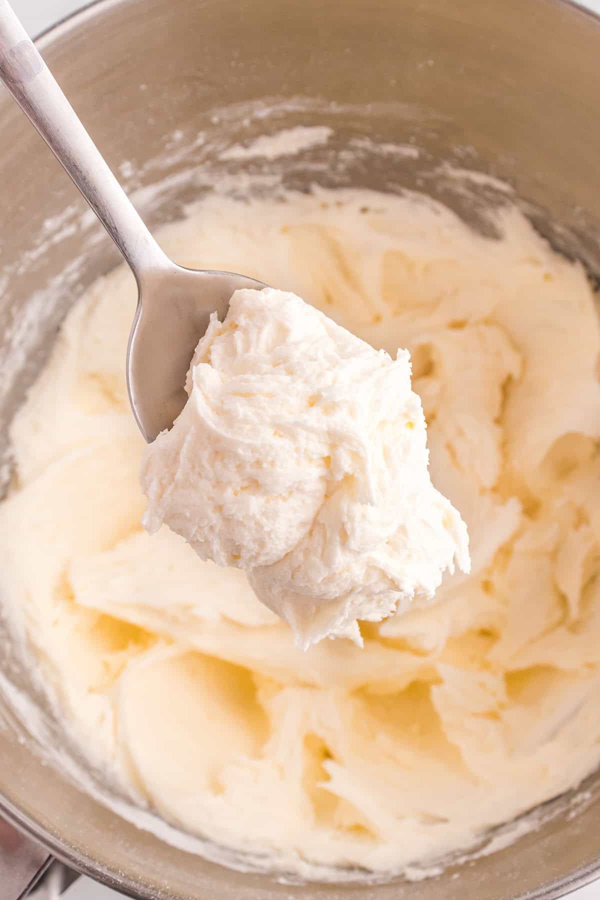 A metal spoon holds a scoop of creamy, whipped marshmallow frosting above a mixing bowl filled with more easy frosting.