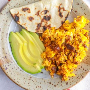 Plate with huevos con chorizo, corn tortilla and sliced avocado