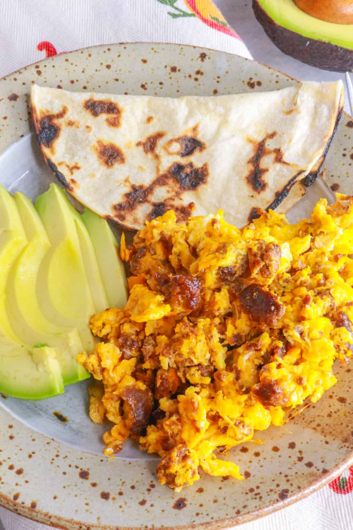 Plate with huevos con chorizo, corn tortilla and sliced avocado