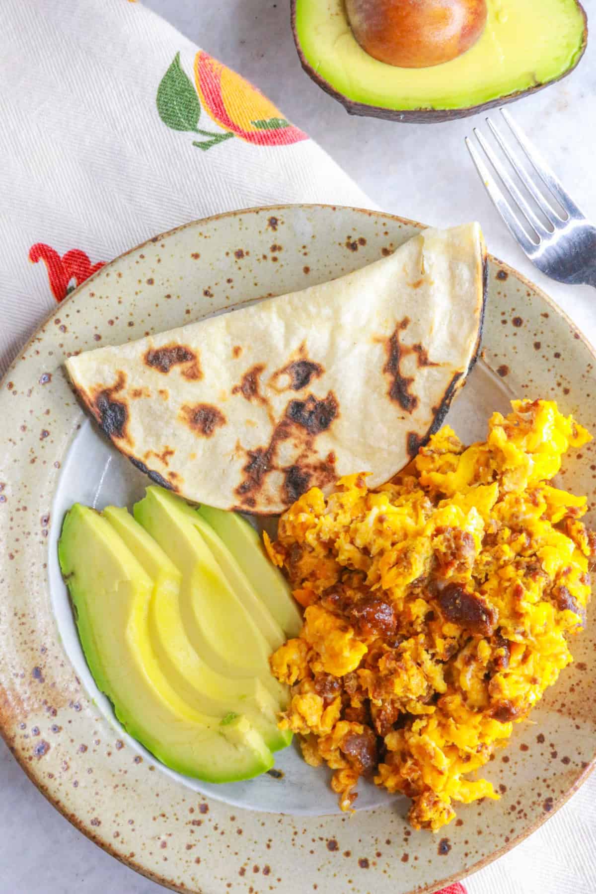 Plate with huevos con chorizo, corn tortilla and sliced avocado