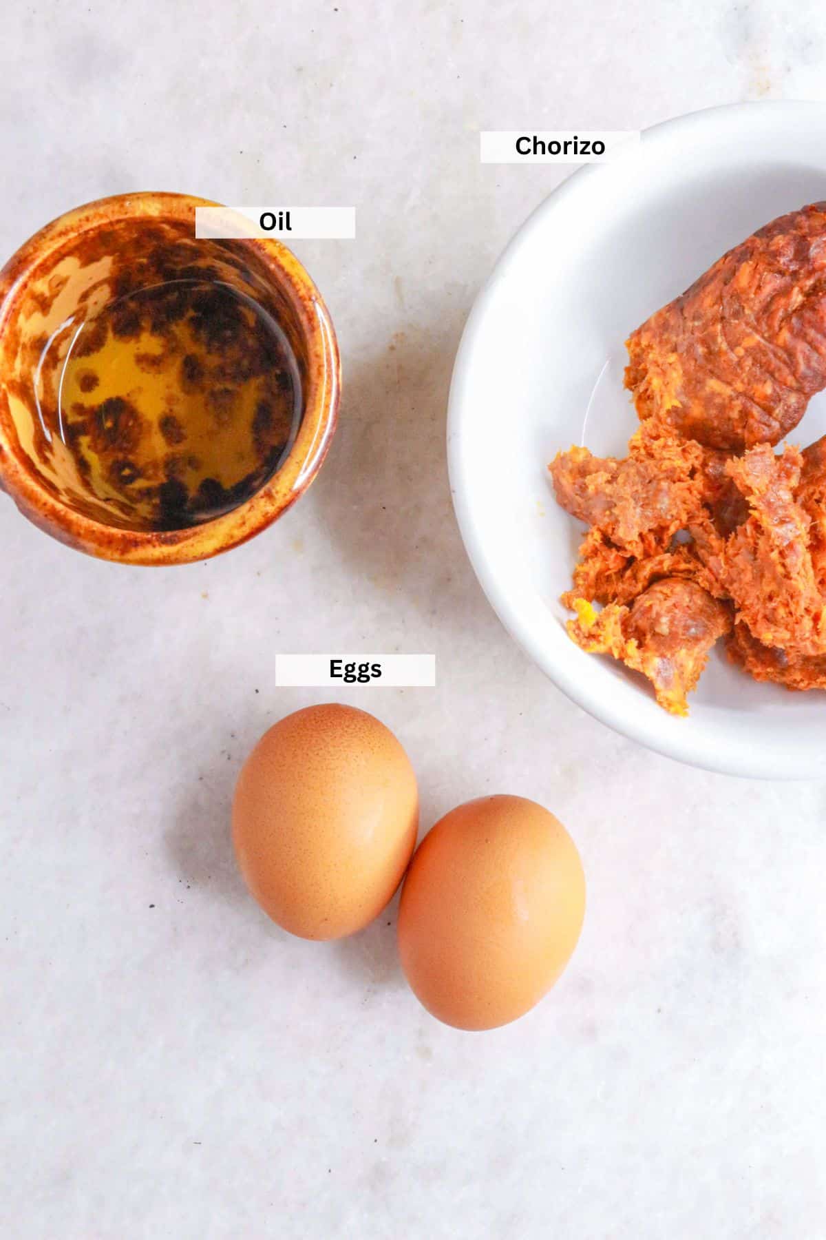 Ingredients for huevos con chorizo: Small bowl with oil, bowl with raw chorizo, 2 eggs