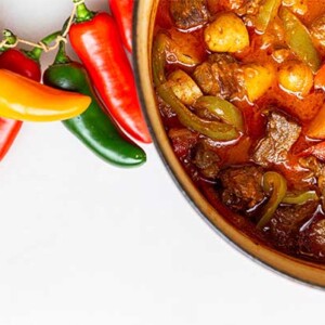 Hungarian Goulash in a pot with fresh peppers next to it on a white background