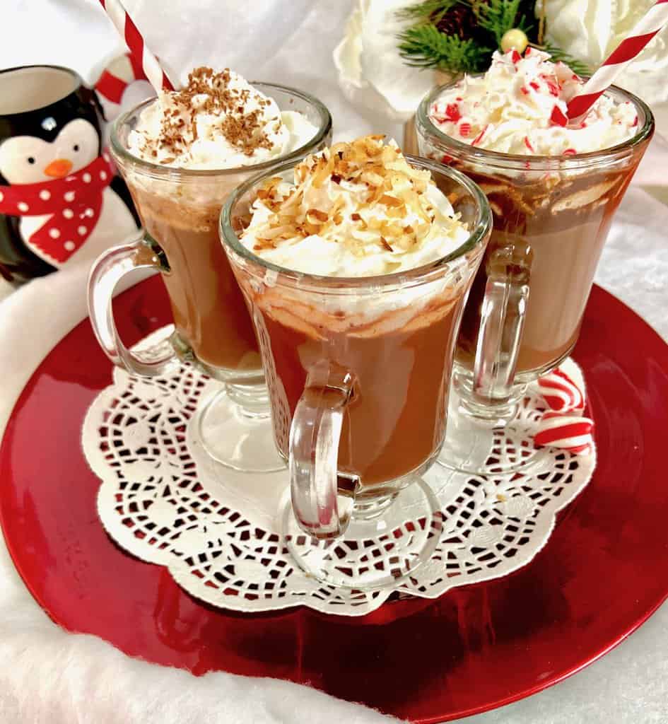 Three glass mugs of hot cocoa on red serving platter.