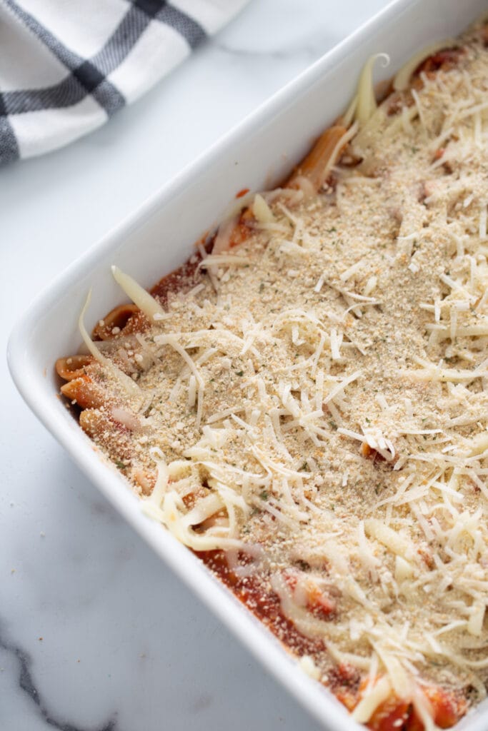 Overhead photo of casserole dish filled with pasta, tomato sauce and shredded cheese, ready for the oven.