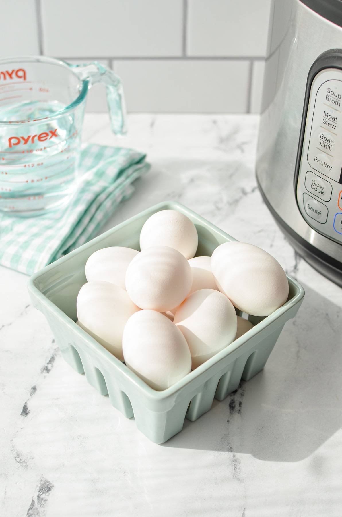 Eggs in a carton with an Instant Pot and measuring cup of water in the background.