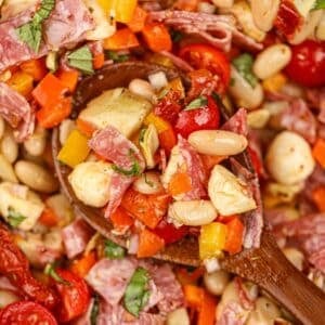 A wooden spoon scooping a portion of bean salad with sun-dried tomatoes, mozzarella, and basil.