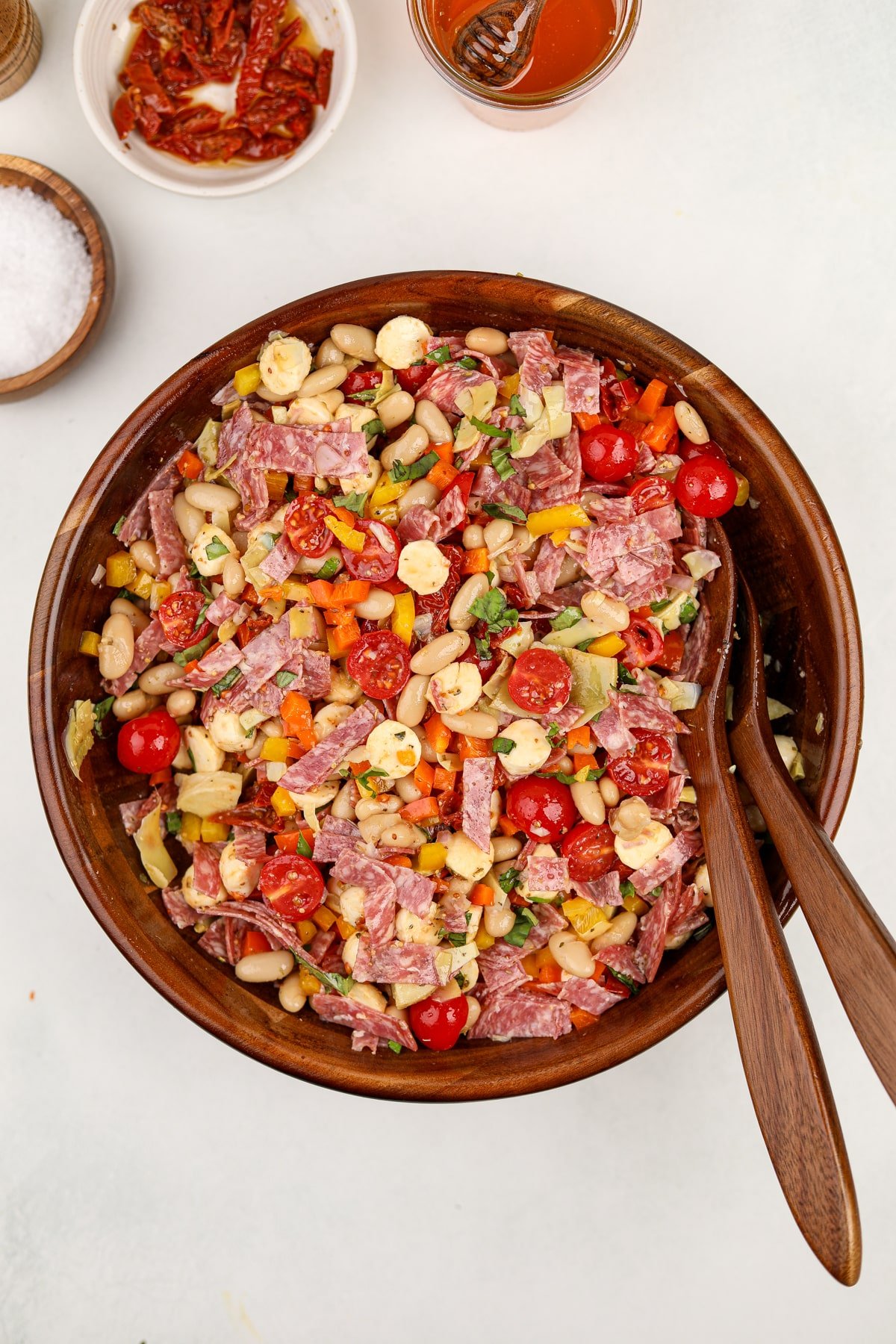 A salad bowl filled with salad featuring white beans, cherry tomatoes, salami, and mini mozzarella balls.