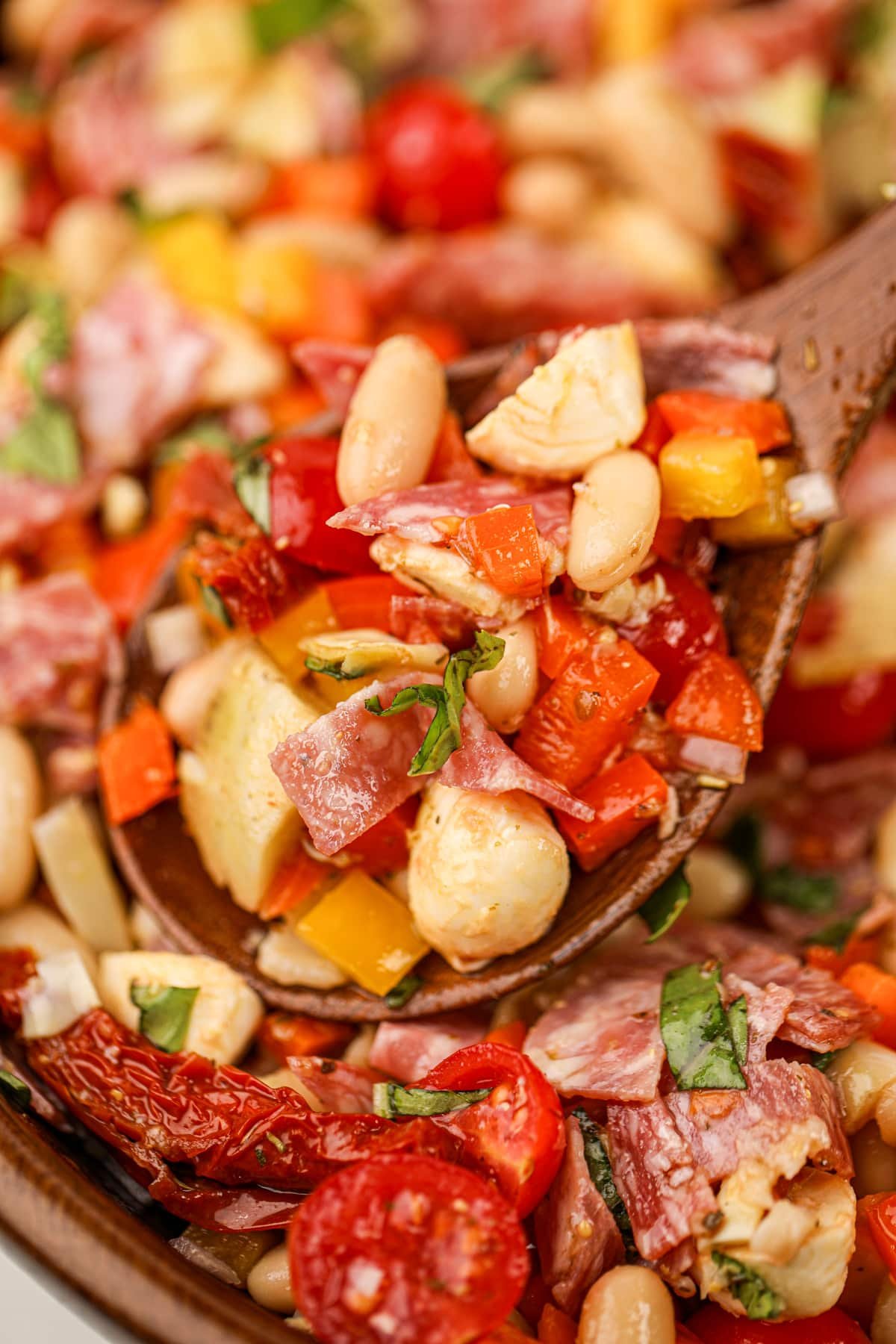 A wooden spoon taking a portion of bean salad from a wooden bowl.
