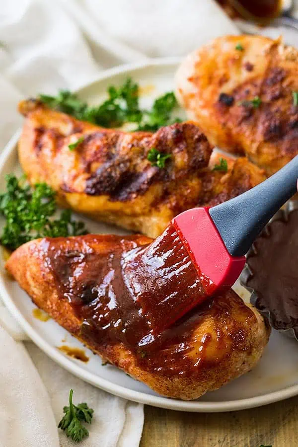 closeup: red kitchen brush sweeping Kansas City barbeque sauce onto chicken breast