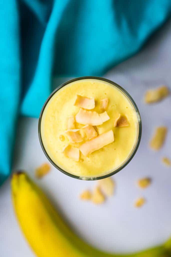 Overhead view of a mango pineapple smoothie garnished with coconut chips