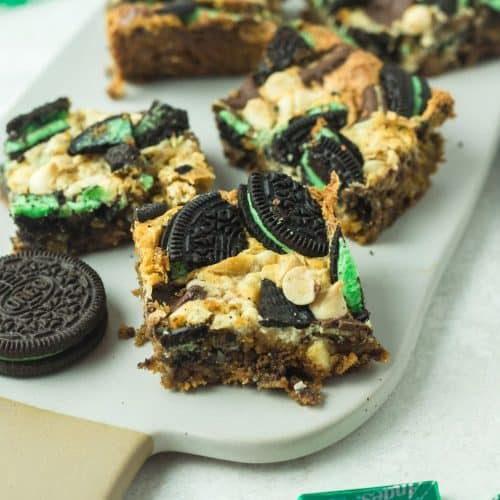 Image of mint cookie bars on a white serving plate with Andes mints and mint Oreo cookies on a side