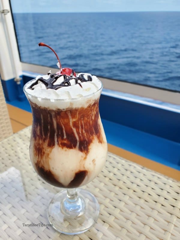 Chocolate ice cream drink in a shake glass next to a window with the ocean behind it