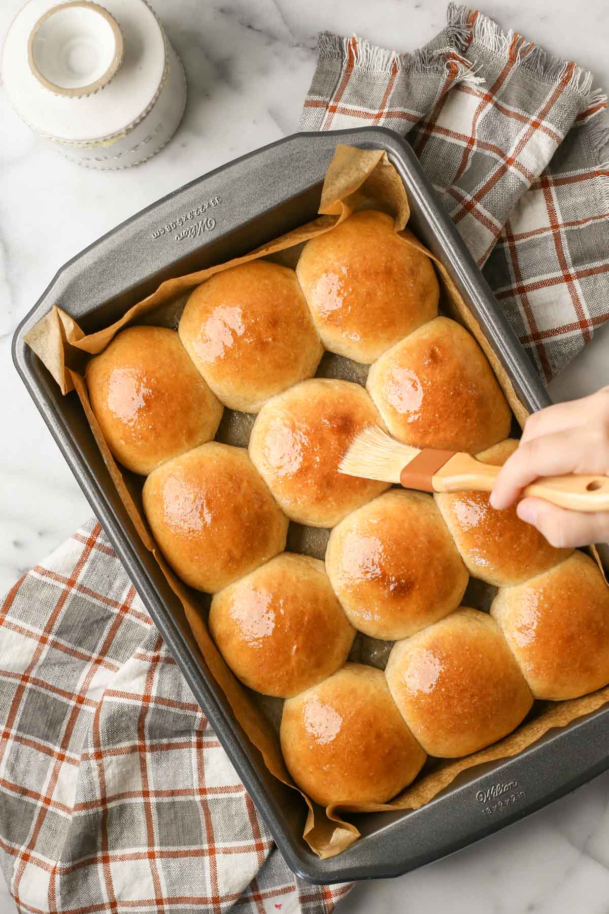 Overhead shot of a baking pan of Overnight Honey Wheat Rolls being brushed with melted butter.