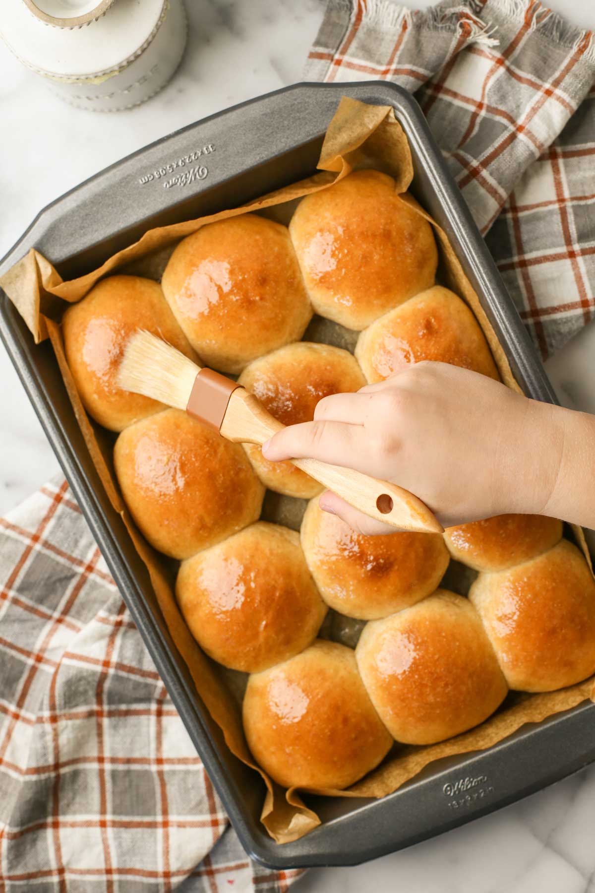 Overhead shot of a baking pan of Overnight Honey Wheat Rolls being brushed with melted butter.