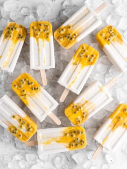 Tropical popsicles featuring mango, passion fruit, and coconut lay on a bed of ice