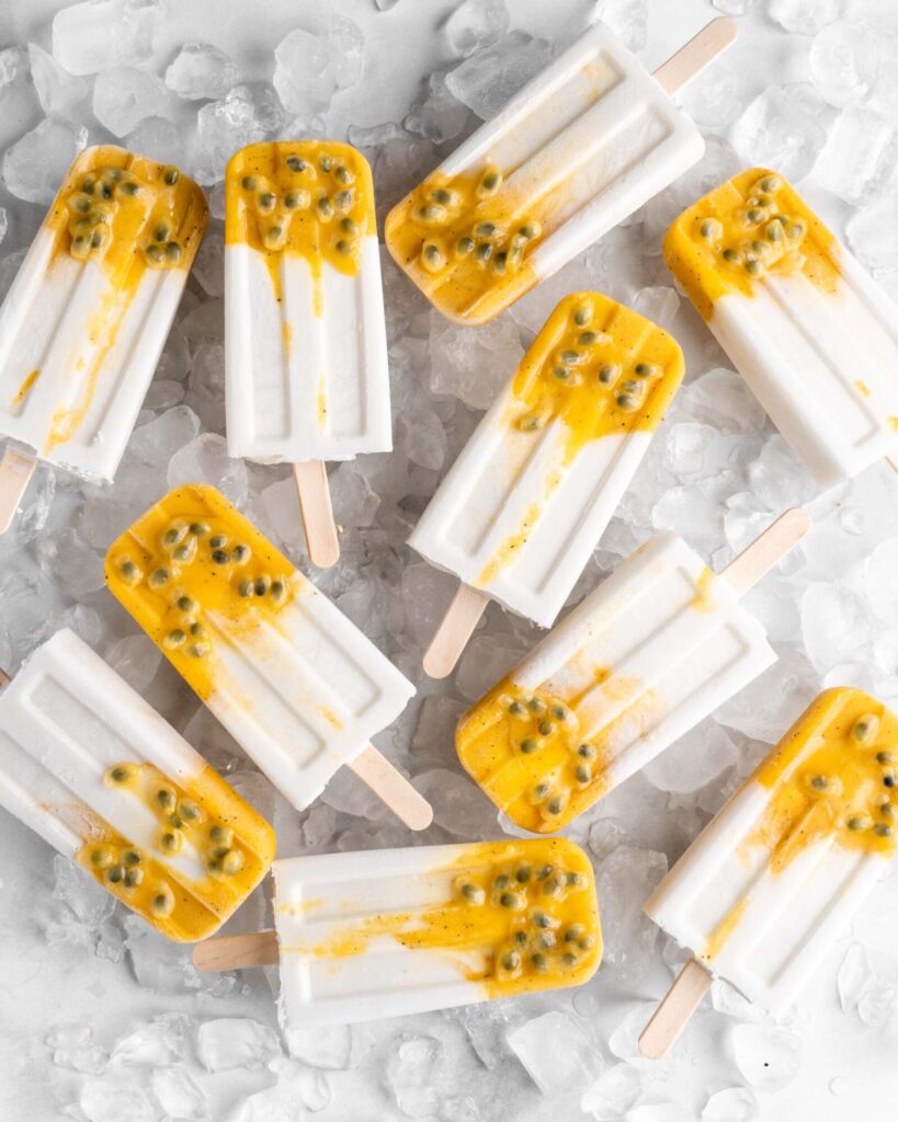 Tropical popsicles featuring mango, passion fruit, and coconut lay on a bed of ice