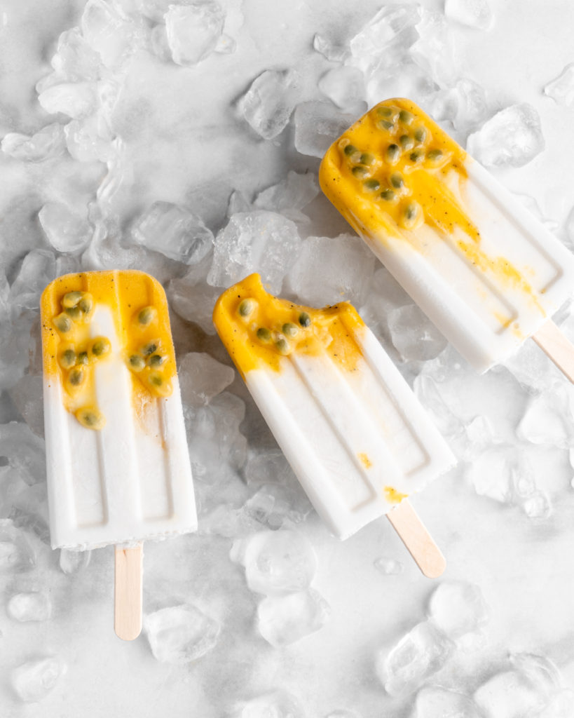 Tropical popsicles featuring mango, passion fruit, and coconut lay on a bed of ice