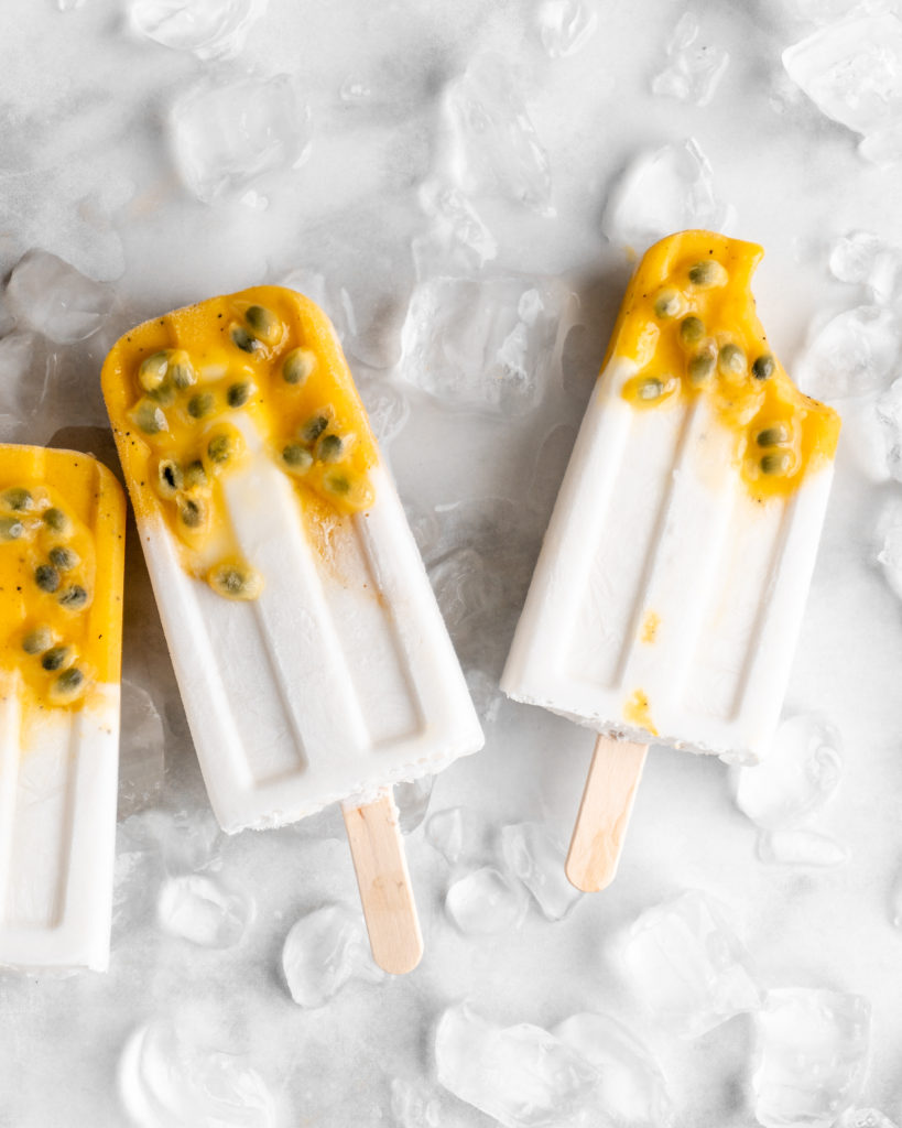 Tropical popsicles featuring mango, passion fruit, and coconut lay on a bed of ice