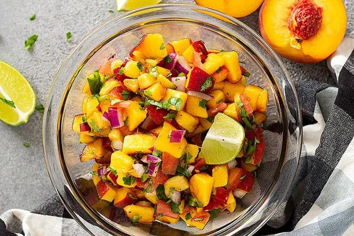 Top down view of peach salsa in a bowl garnished with fresh lime and cilantro. 