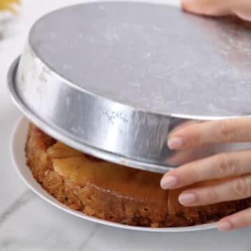 Baked cake being flipped onto a white serving dish. 