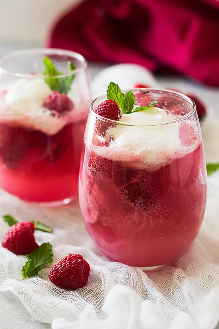 Two full glasses of pink champagne, raspberry sherbet, pineapple juice, and sprite. They are also topped with freshly whipped cream. 