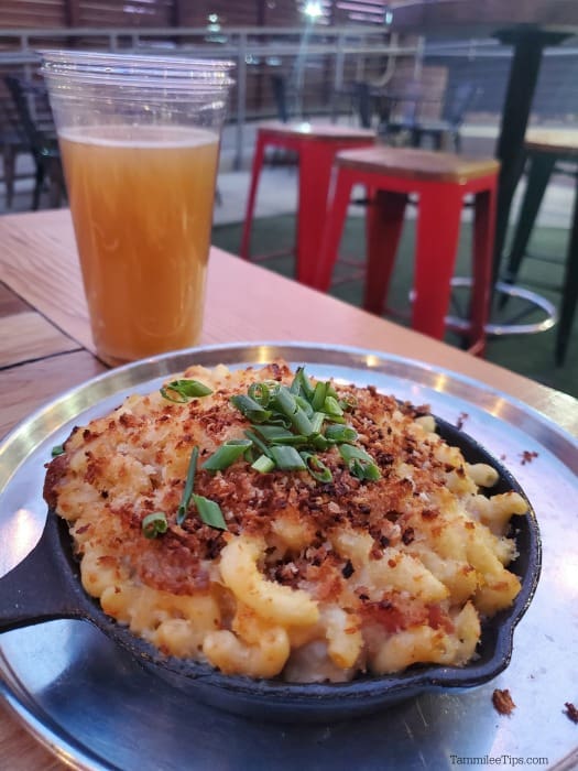mac and cheese in a skillet next to a glass of beer on a picnic table 