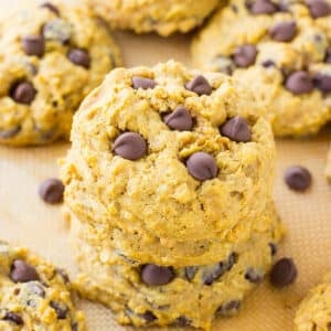 Pumpkin oatmeal cookies stacked up on a baking tray with more behind.