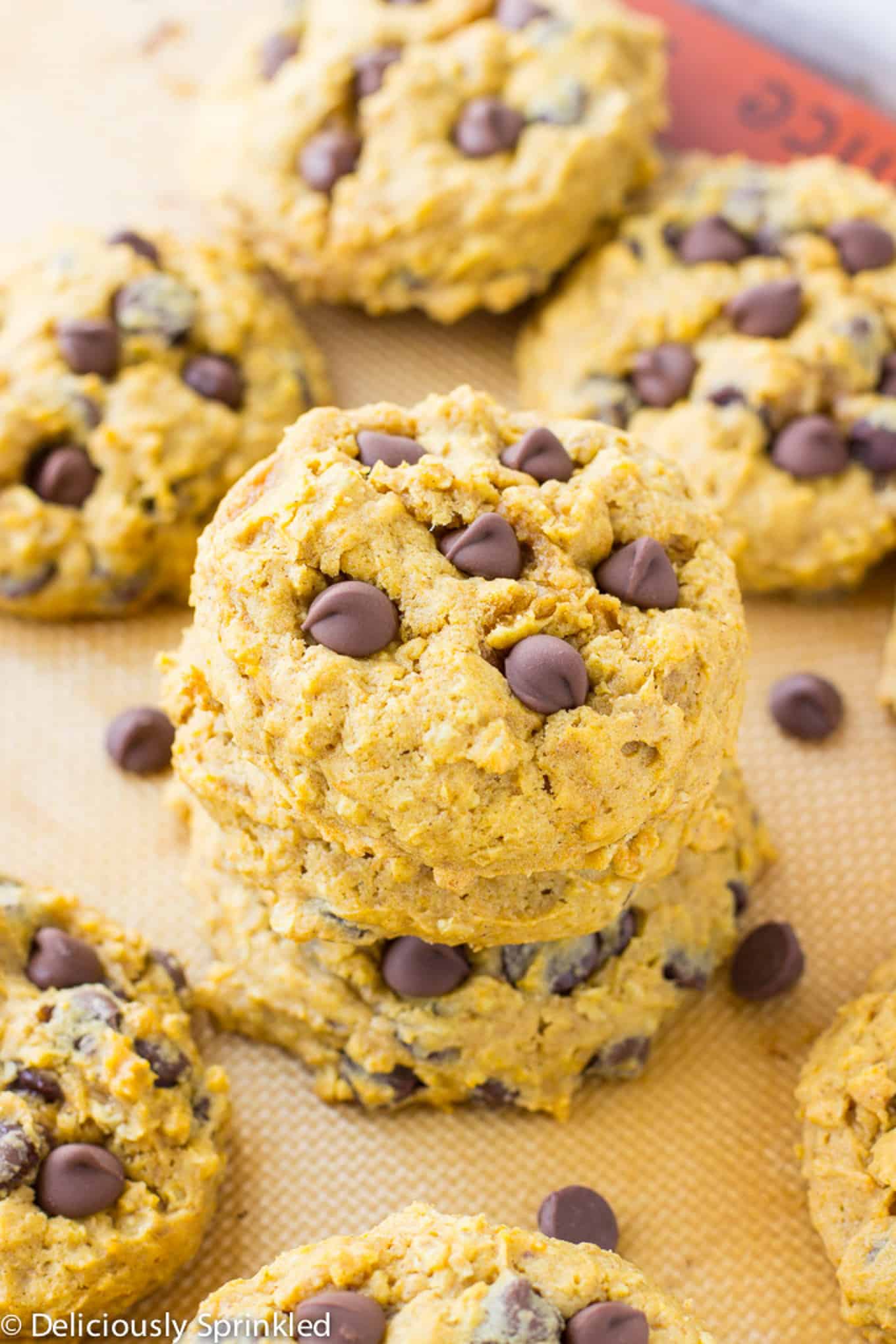 A stack of pumpkin oatmeal cookies with chocolate chips on the baking tray with more in the background.