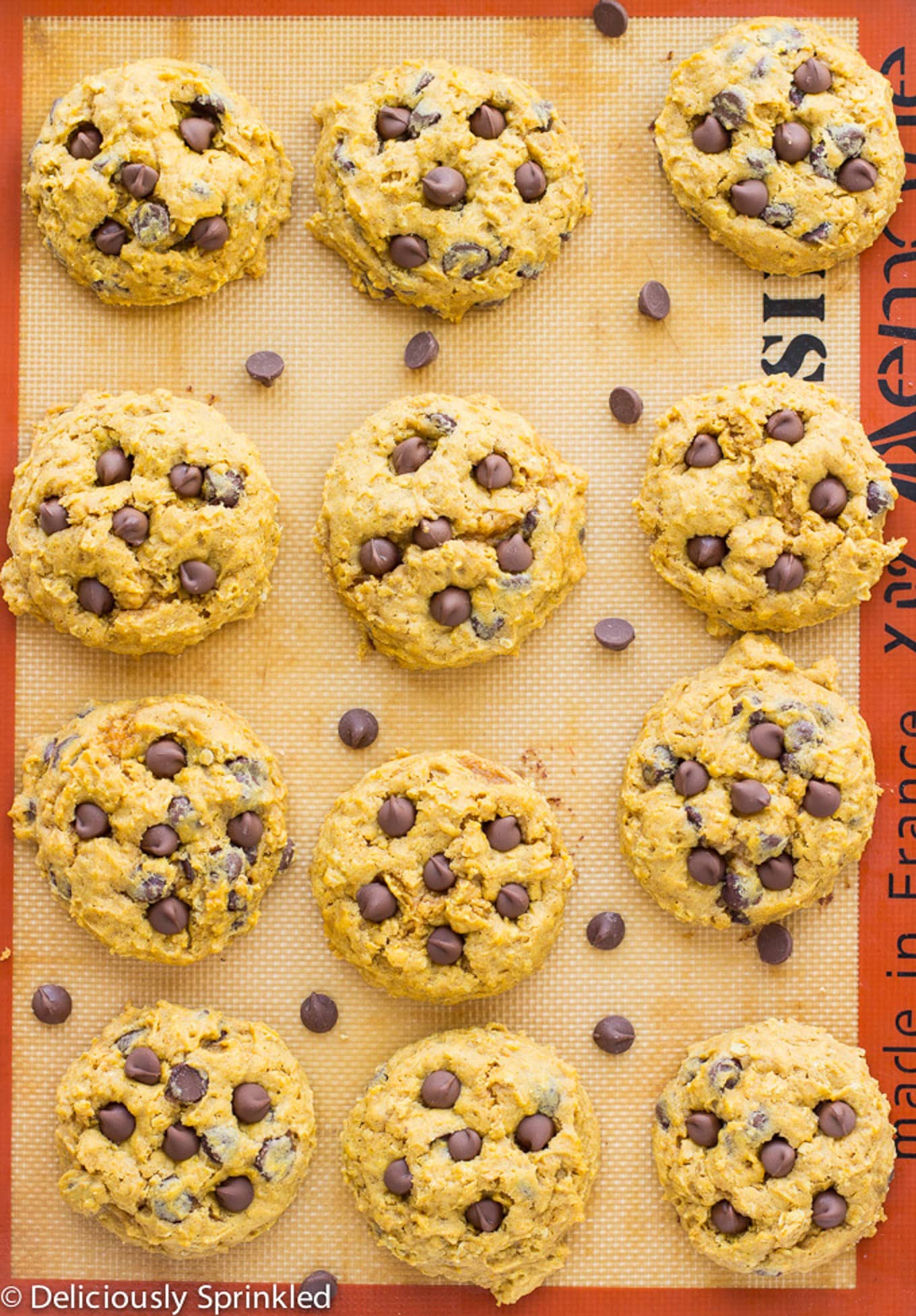 Soft pumpkin cookies on a silpat on a baking tray after cookie with chocolate chips spilled on the tray.