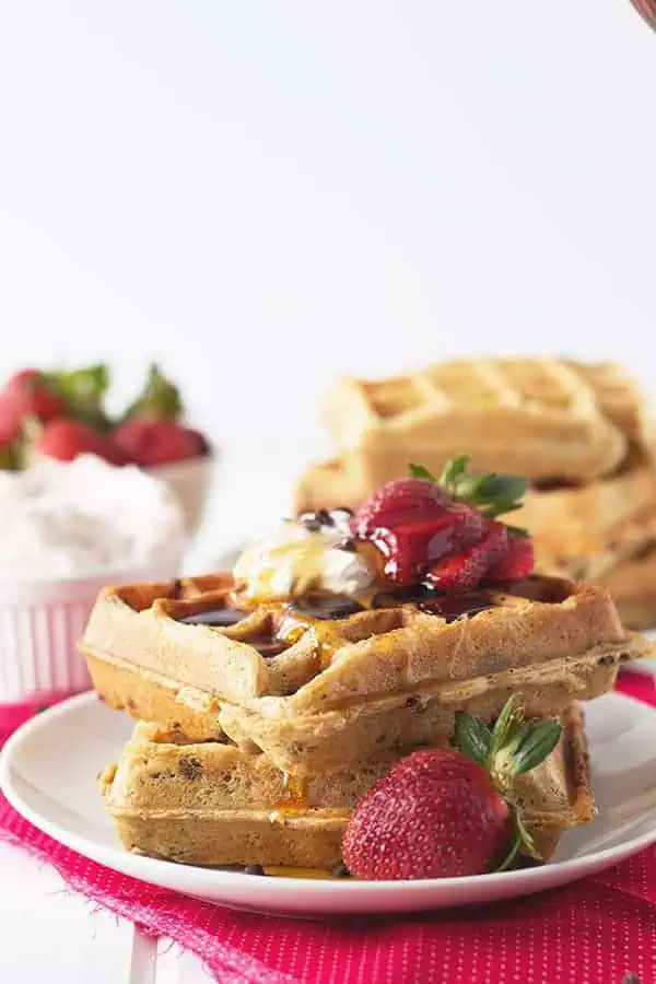 a stack of my recipe for strawberry waffles with syrup, whipped cream, and fresh berries on top
