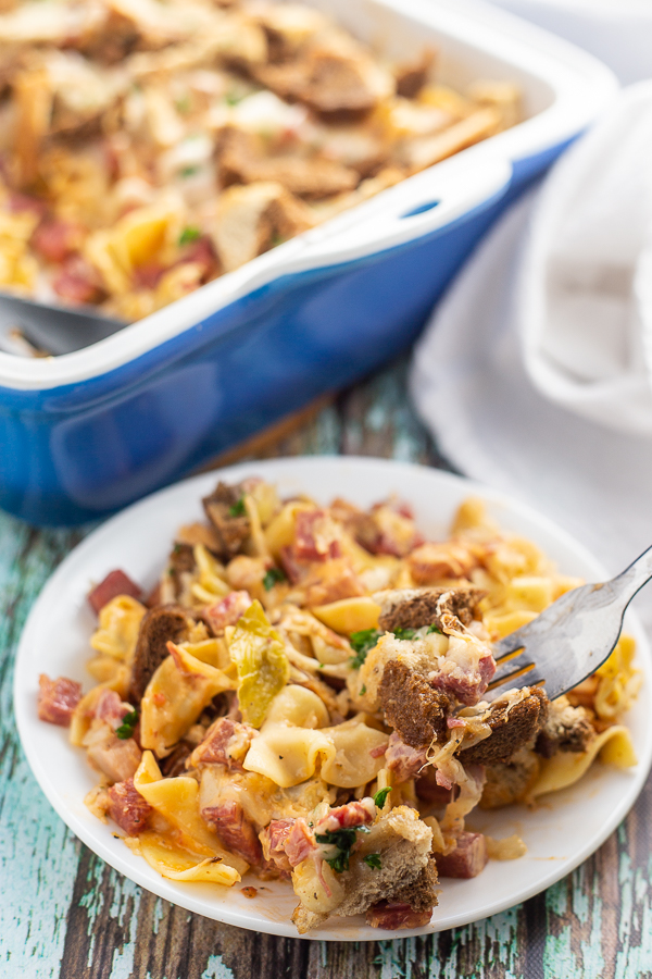 Reuben Casserole on a white plate with fork in it and blue casserole dish in the background