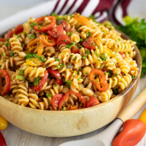 Romesco pasta salad in a wooden bowl topped with freshly chopped parsley and a linen napkin behind.