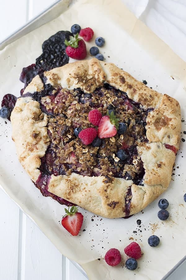 a galette on a parchment lined baking sheet with juicy berries in it and around it