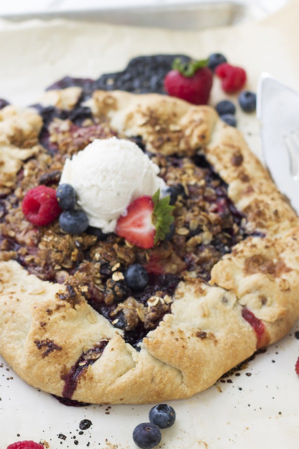 a berry galette on a baking sheet with fresh berries and vanilla ice cream on top 