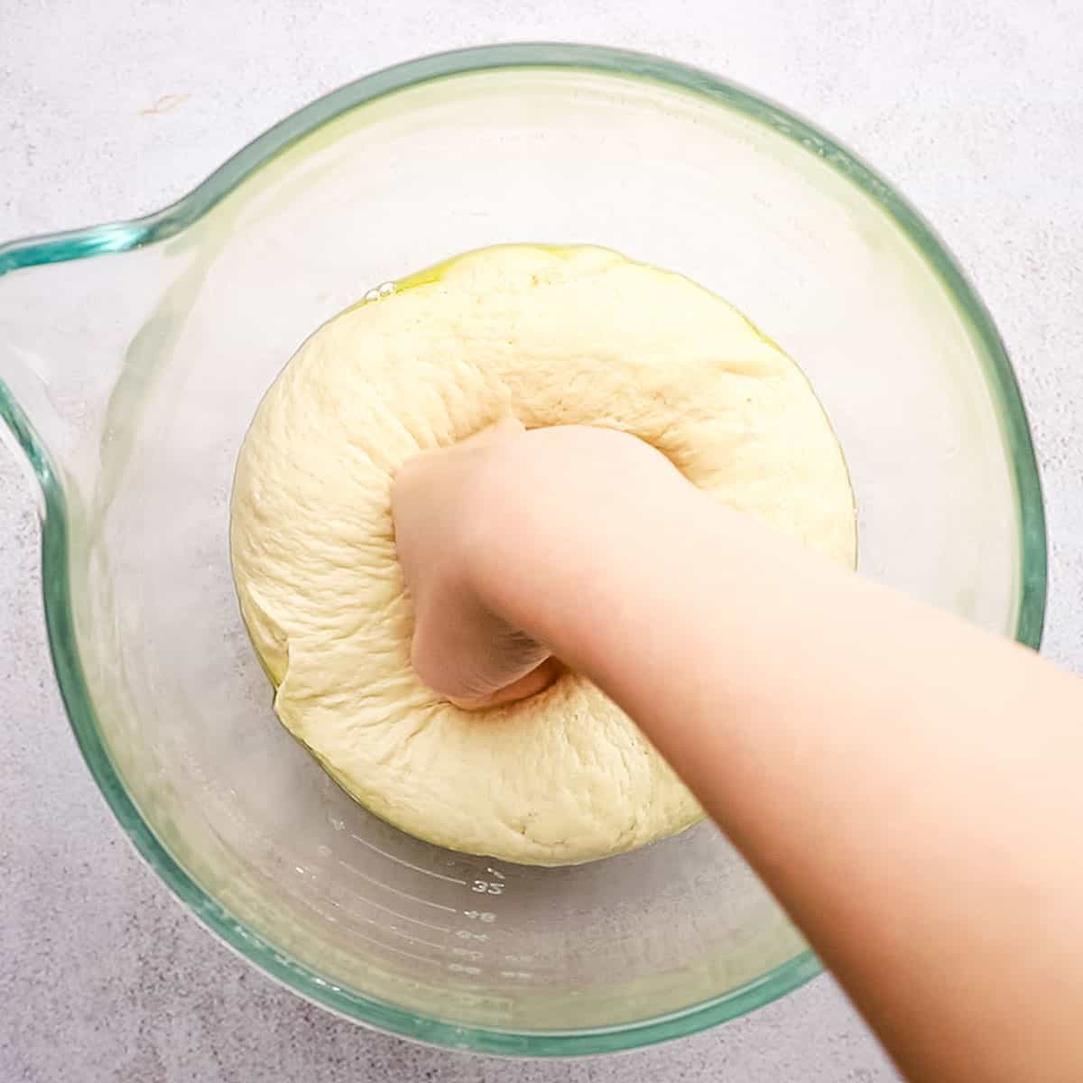 Risen pizza dough being punched down to deflate.