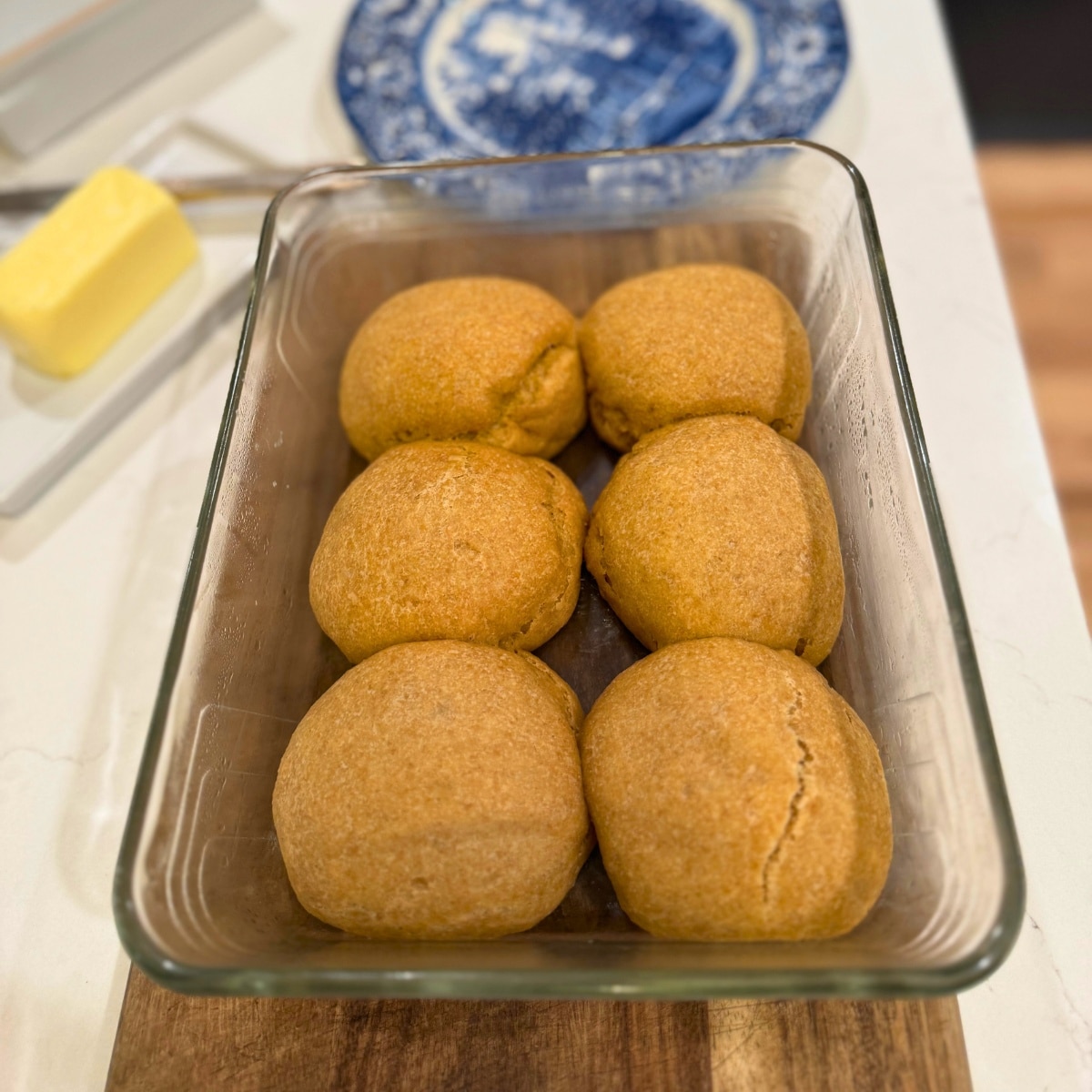 soft einkorn sourdough rolls in pan on cutting board by butter and plate