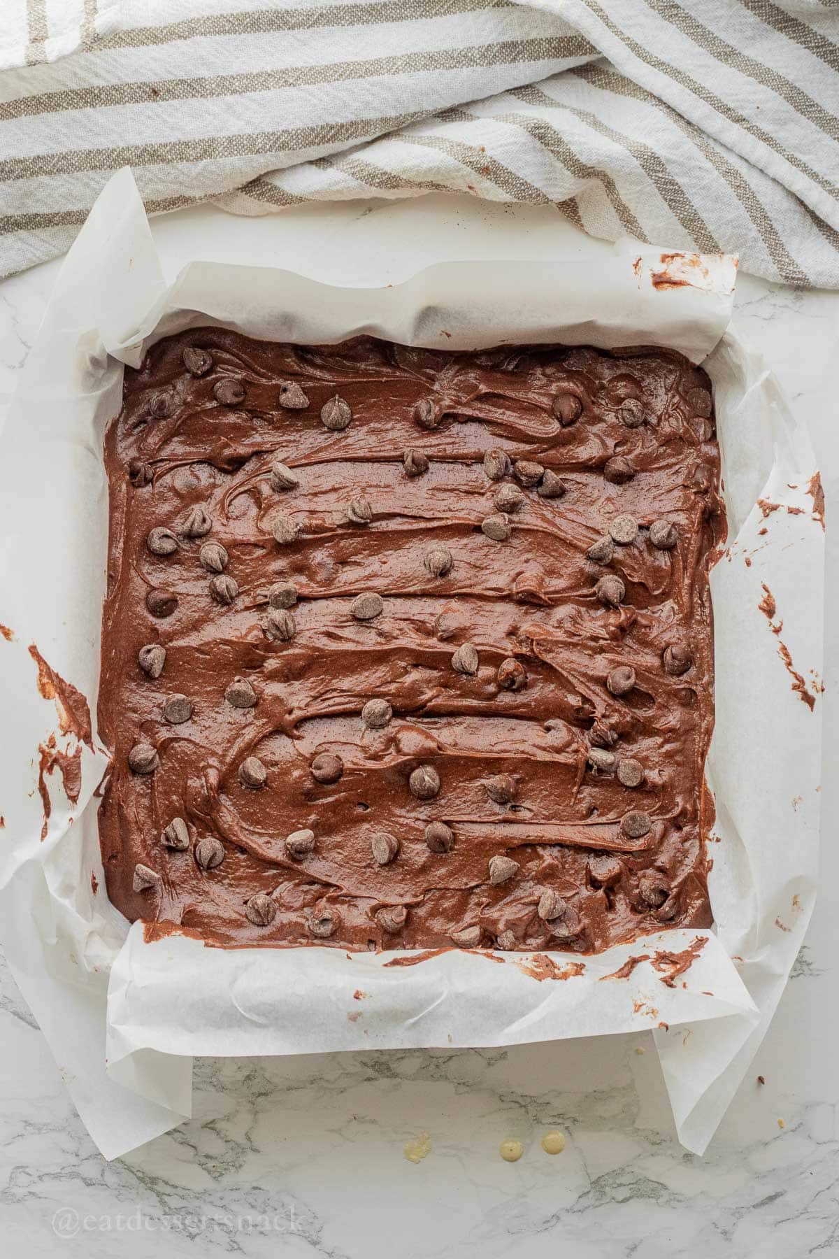 Raw discard brownie batter in parchment paper lined baking pan with chocolate chips on top.