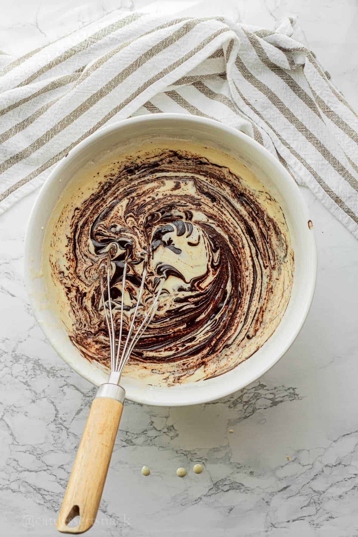 Mixing cocoa powder and butter into wet ingredients in white bowl.