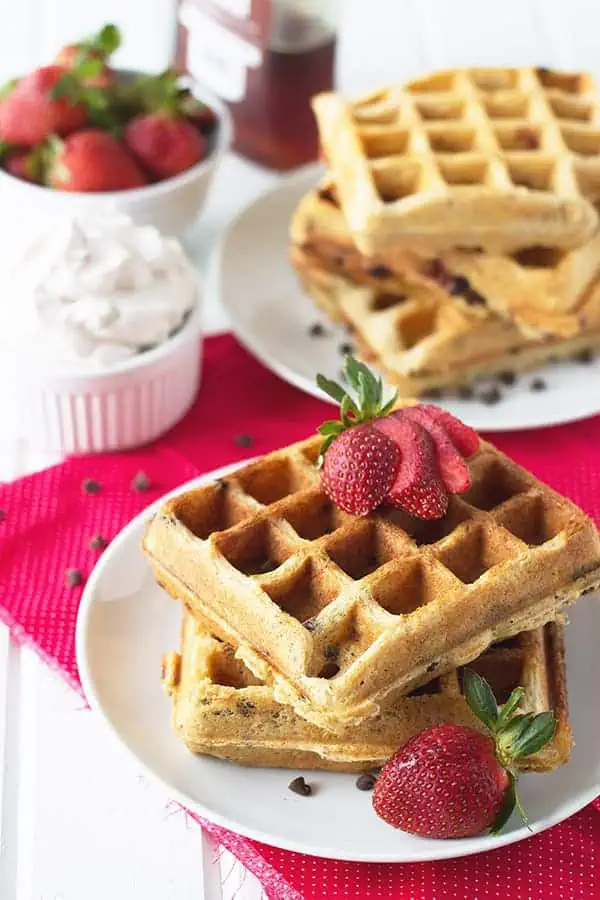 2 strawberry waffles on a plate with fresh strawberries as a garnish