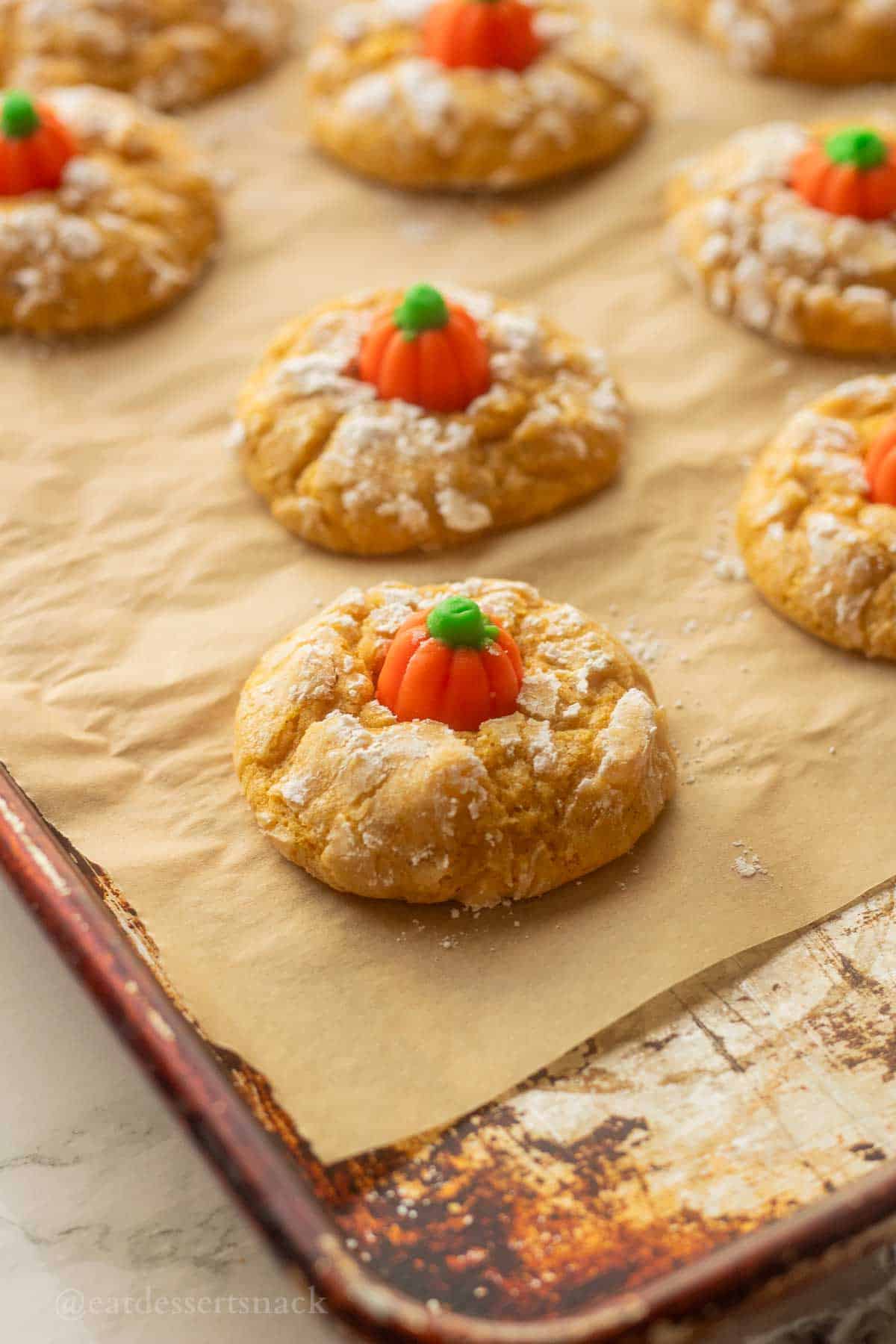 Baked pumpkin sugar cookies on parchment paper on metal pan.